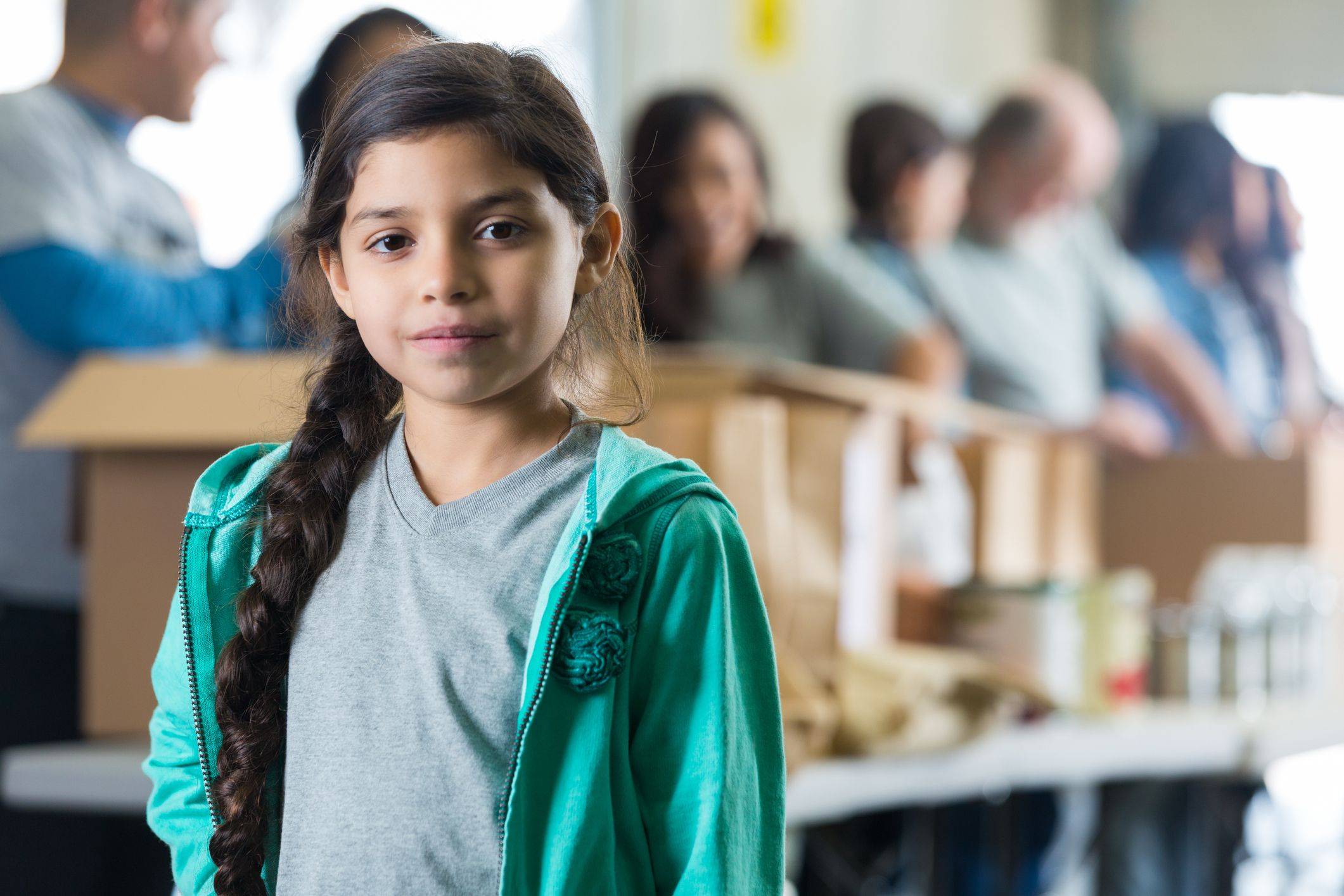 Serious Hispanic child in front of volunteers sorting food donations
