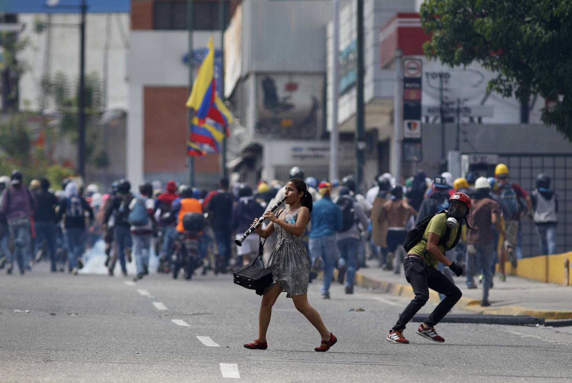 Una mujer joven toca su clarinete en medio de enfrentamientos entre manifestantes antigubernamentales y fuerzas de seguridad, durante una protesta en Caracas, Venezuela, hoy jueves 6 de julio de 2017. (Foto AP / Ariana Cubillos)