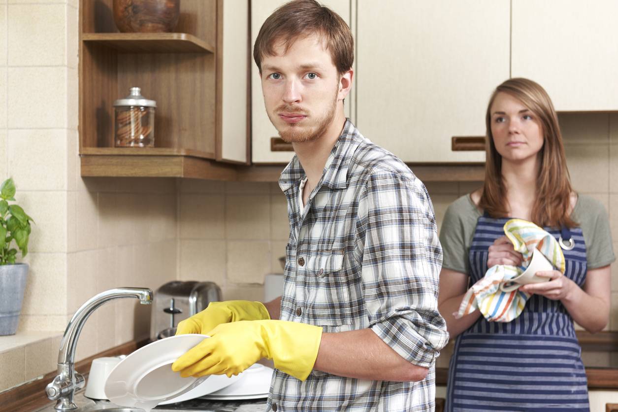 Man Reluctantly Washing Up In Kitchen With Partner
