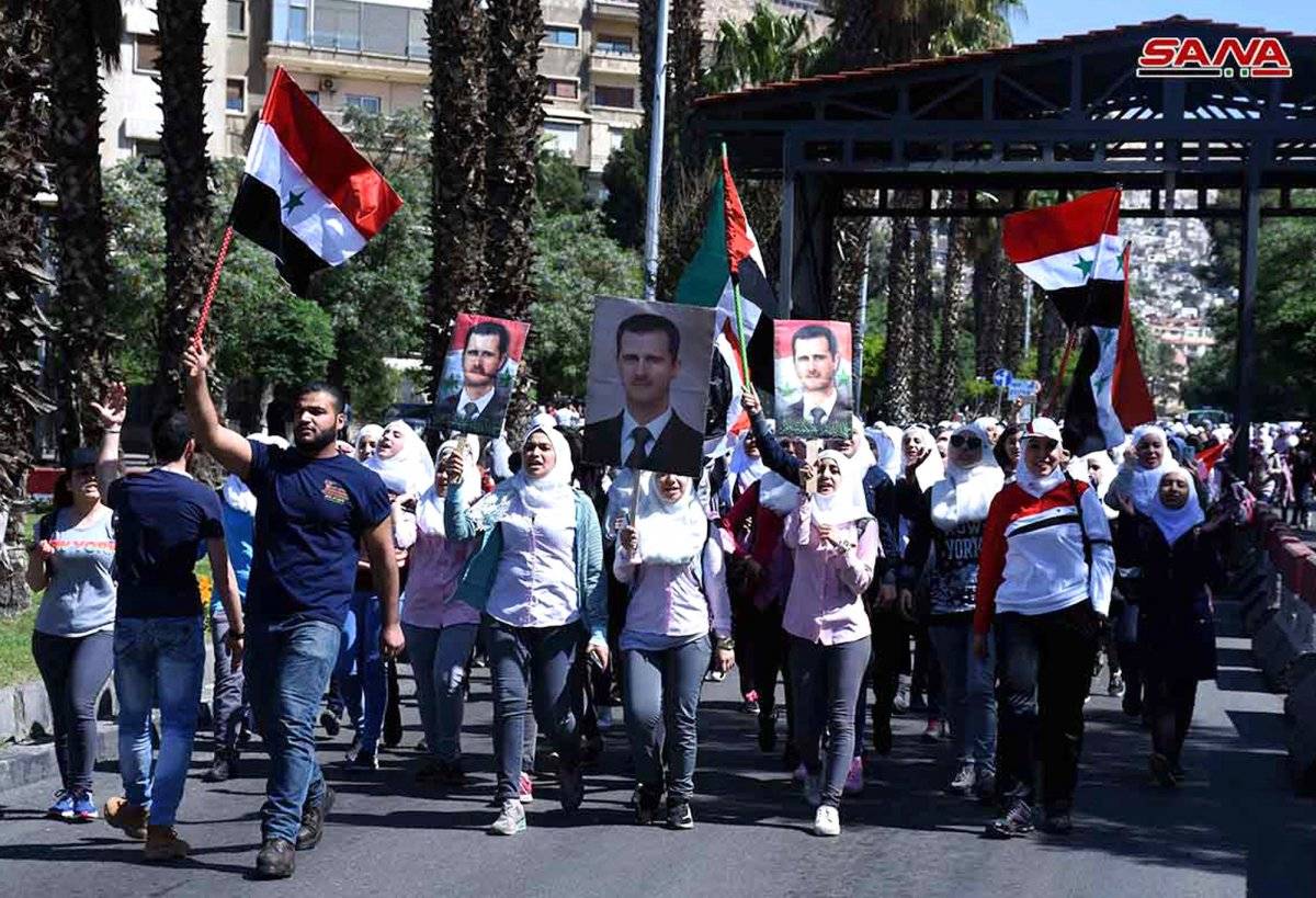 En esta imagen, distribuida por la agencia de noticias oficial de Siria, SANA, manifestantes sostienen banderas del país y retratos del presidente Bashar Assad durante una manifestación en apoyo de las fuerzas armadas sirias, en Damasco, el 16 de abril de