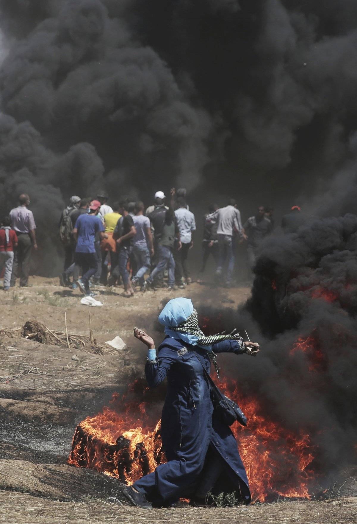 Una mujer palestina arroja piedras contra las tropas israelíes durante una protesta en la frontera de la Franja de Gaza con Israel, el lunes 14 de mayo de 2018. El fuego israelí ha matado a decenas de palestinos durante protestas masivas a lo largo de la