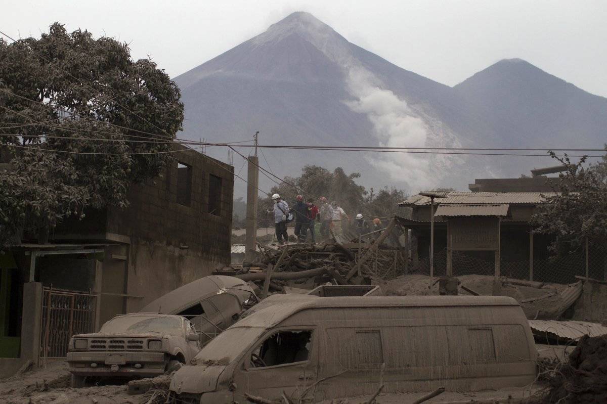 Rescatistas caminan por los tejados de Escuintla, Guatemala, el lunes 4 de junio de 2018, cubierto con cenizas pesadas arrojadas por el Volcán de Fuego, o "Volcán de fuego", en el fondo, en el centro izquierdo. (Foto AP / Luis Soto)