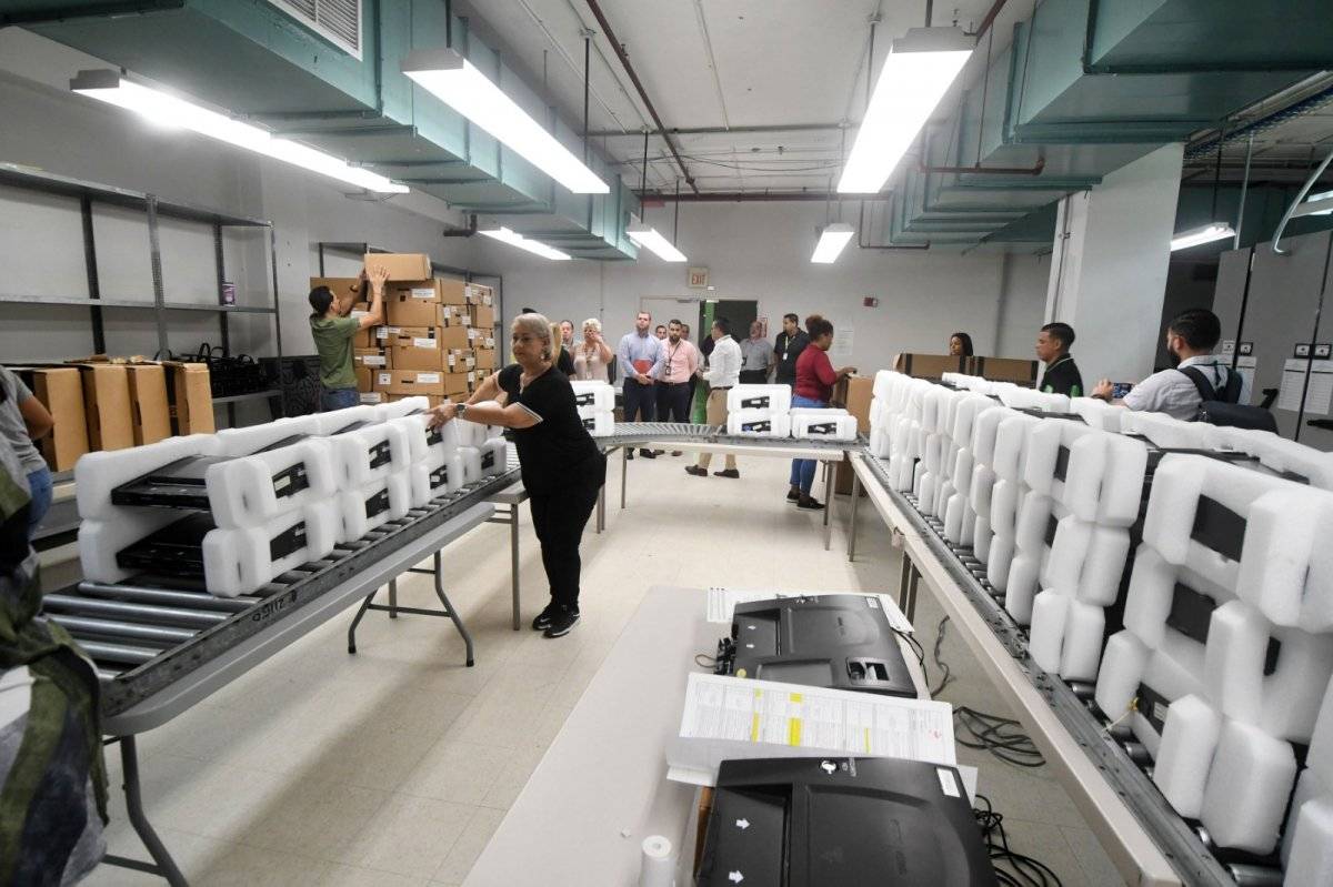 Empleados de la CEE trabajan en la fase uno y dos del proceso de mantenimiento de las máquinas de escrutinio electrónico. / Foto: Dennis Jones