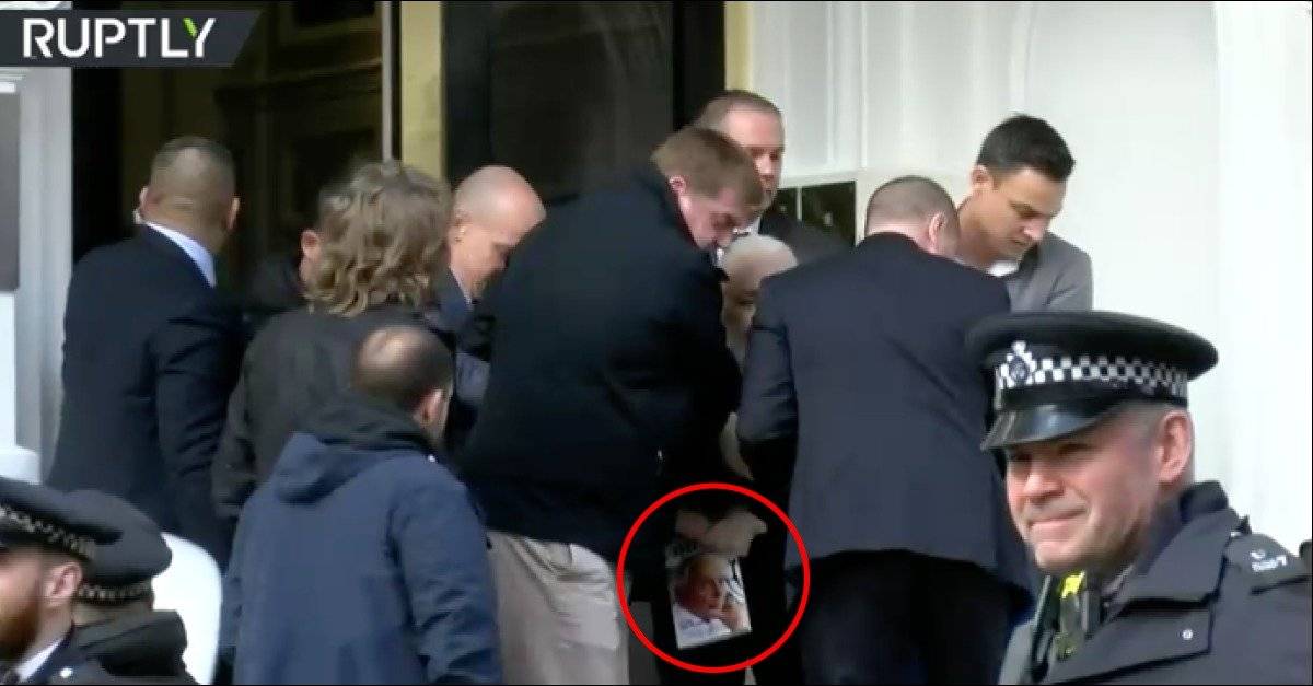 Assange con un libro mientras sale de la embajada