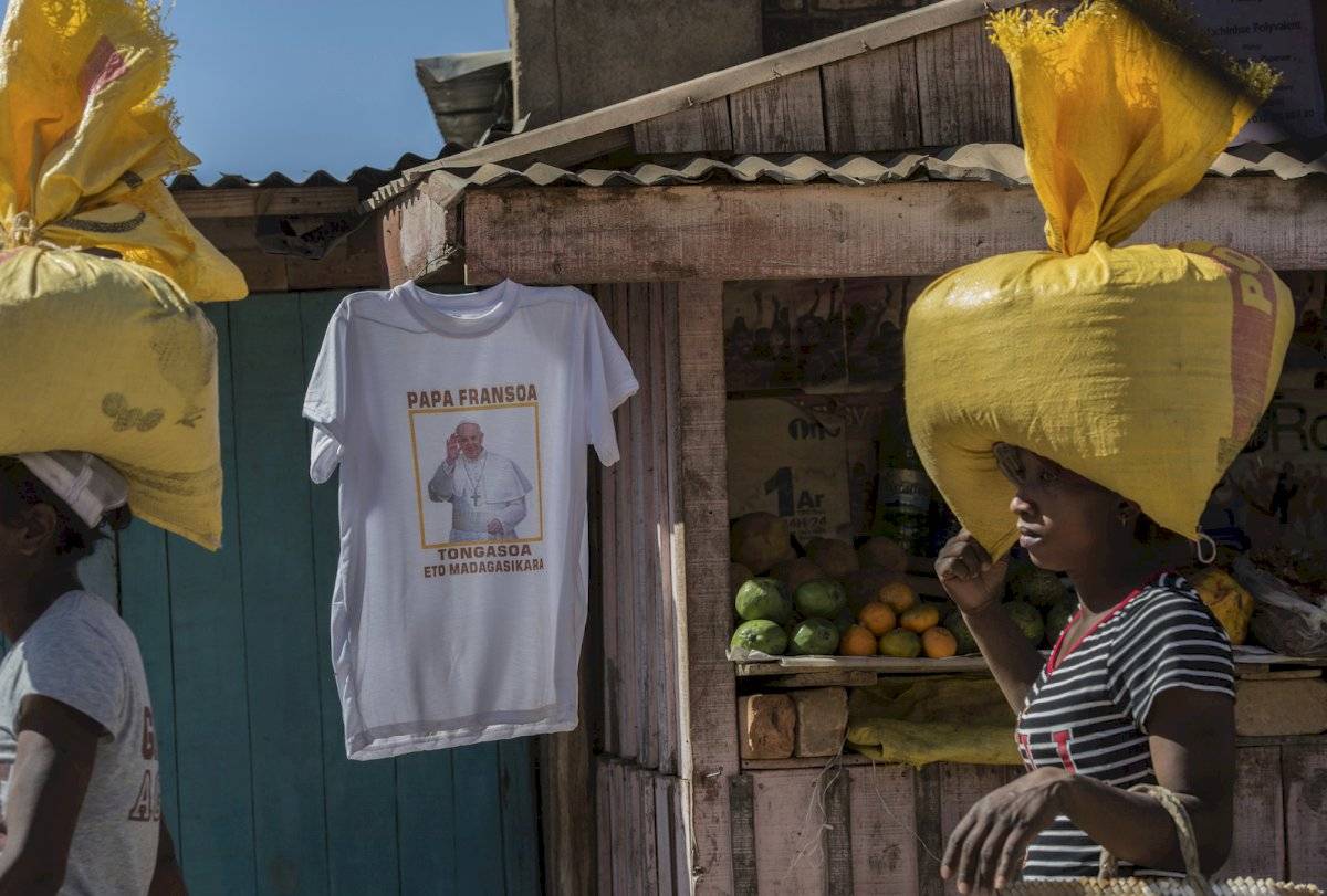 Mujeres con bolsas en sus cabezas pasan por un puesto que vende camisetas del Papa Francisco conmemorando su visita a Madagascar