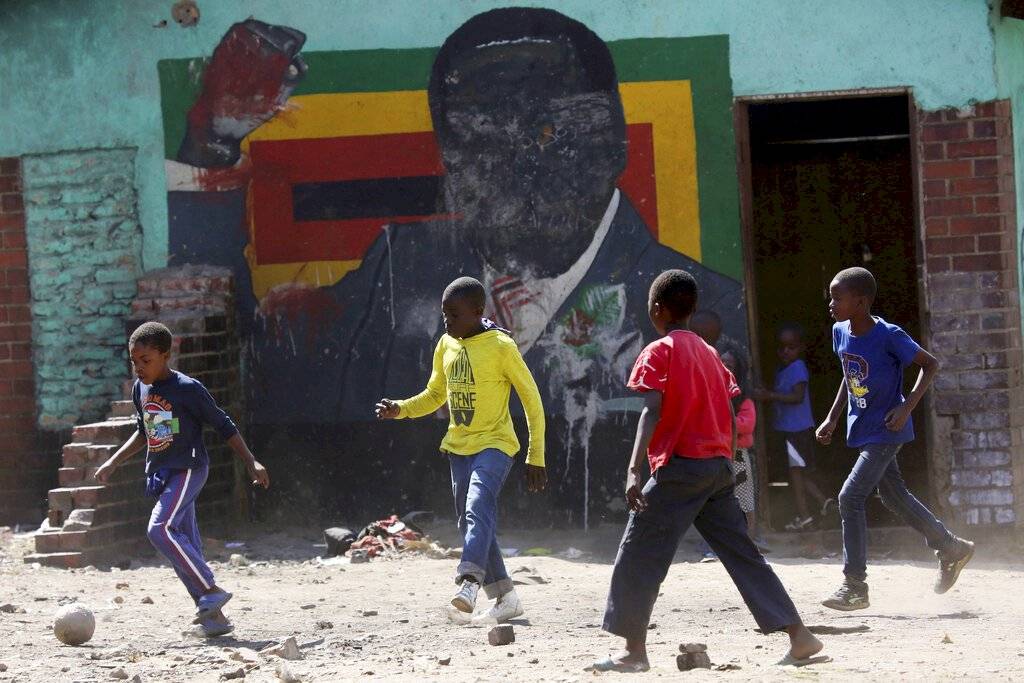Niños juegan fútbol junto a un retrato desfigurado del ex presidente zimbabuense Robert Mugabe en Harare, el viernes 6 de septiembre de 2019, día en que falleció a los 95 años.