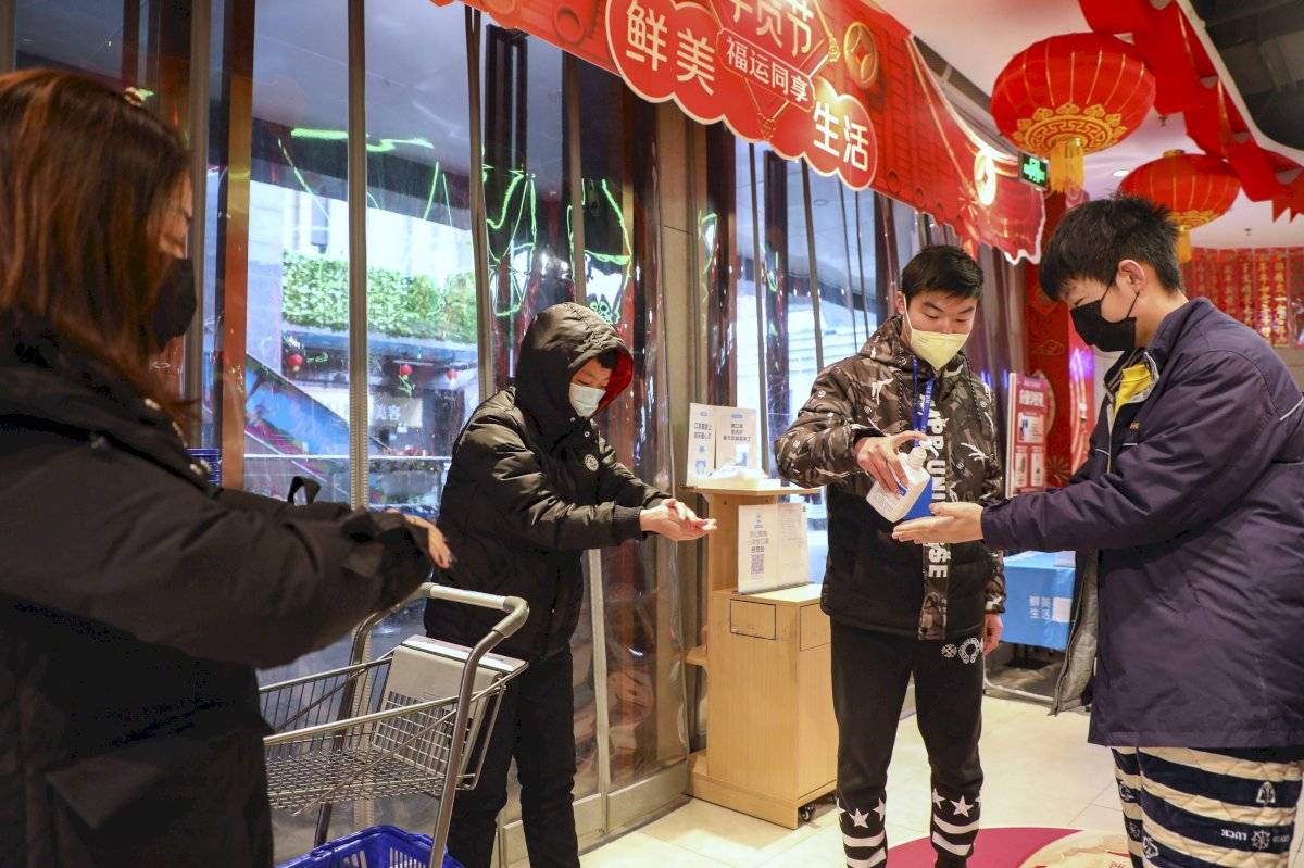 Entrada de mercado en Wuhan, y en la entrada un trabajador dando gel antibacterial a clientes.