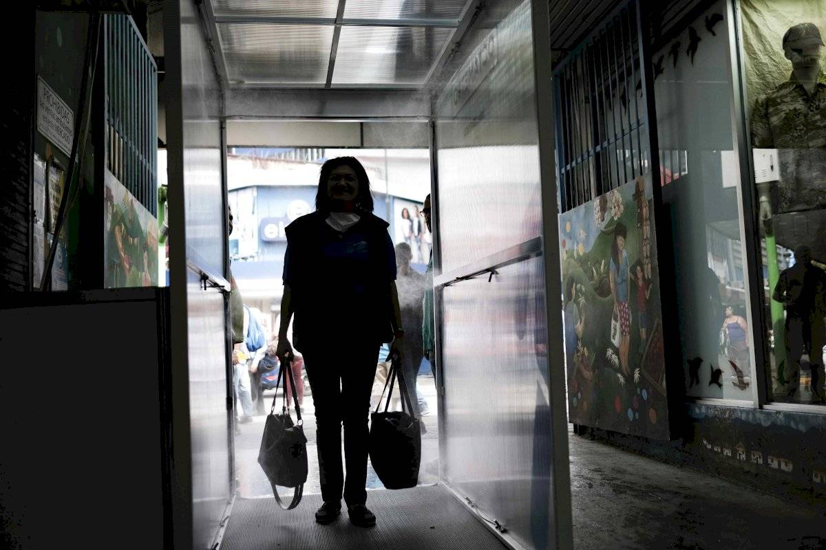Ciudadanos ingresan este jueves a una cabina desinfectante, la primera que se coloca en el país costarricense, para prevención contra la COVID-19, en el mercado central de San José