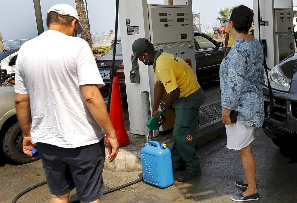Ciudadanos libaneses miran a un trabajador de una estación de servicio, al centro, llenar de gasolina en su bidón para alimentar el generador de su casa mientras la electricidad permanece apagada unas 20 horas al día