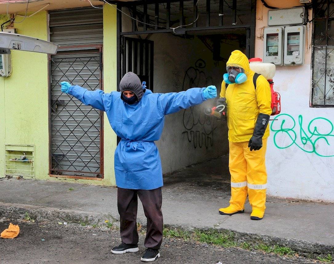 Personal Sanitario utiliza trajes especiales para evitar el contagio de la COVID-19 mientras desinfectan a una persona en una calle de Quito