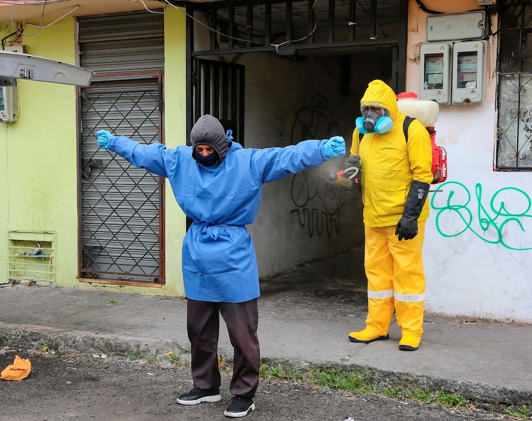 Personal Sanitario utiliza trajes especiales para evitar el contagio de la COVID-19 mientras desinfectan a una persona en una calle de Quito