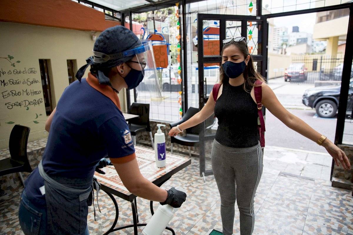 Una mujer aplica alcohol a una cliente antes de entrar a un establecimiento para contener el contagio de la COVID-19 el 07 de julio de 2020 en Quito
