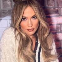 Jennifer Lopez hermosa en un pantalón de mezclilla a la cadera y mini top tejido modelando los zapatos de su colección