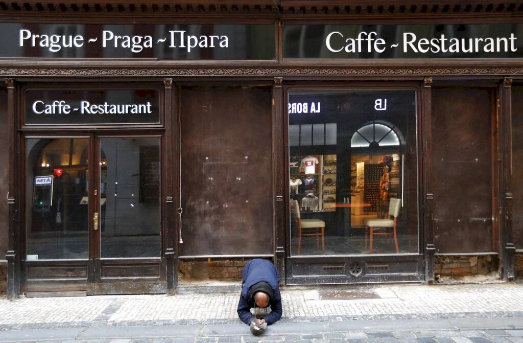 Un mendigo se arrodilla frente a un restaurante cerrado en el centro de Praga, República Checa