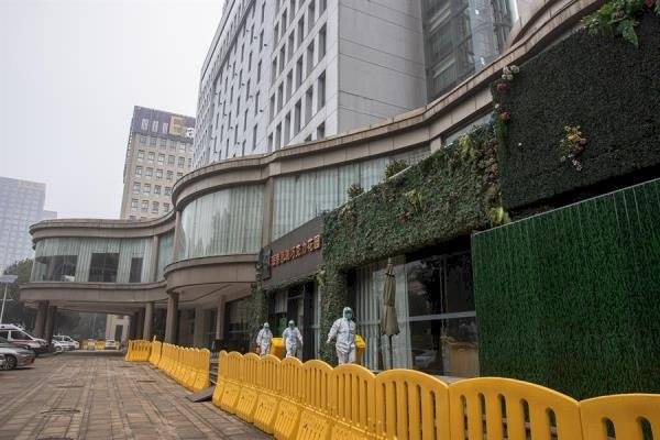 rabajadores con equipo de protección caminan junto al hotel Jade Boutique, donde los miembros del equipo de la OMS